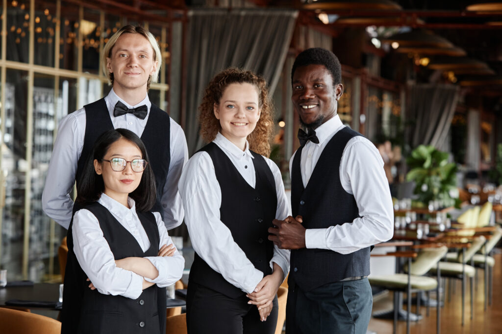Diverse group of servers wearing classic tuxedo uniform smiling at camera